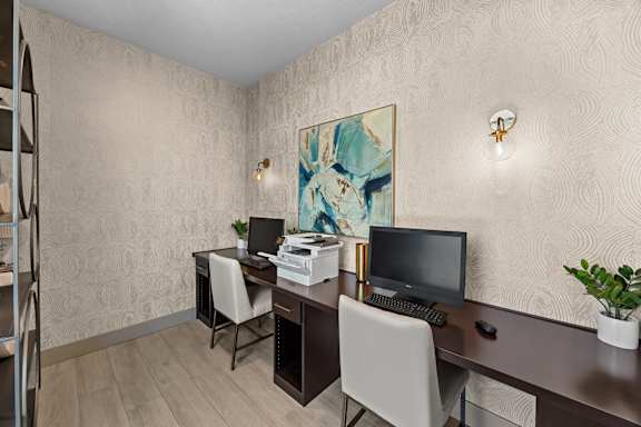 A room with a desk, chairs, and a painting on the wall.