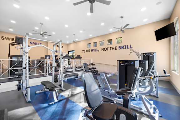 A gym with a variety of equipment including a squat rack, leg press machine, and a bench press.