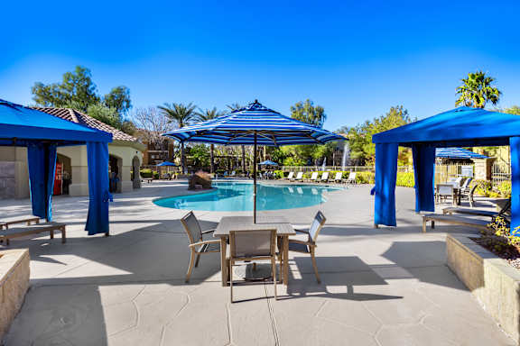 A pool area with a table and chairs under a blue canopy.