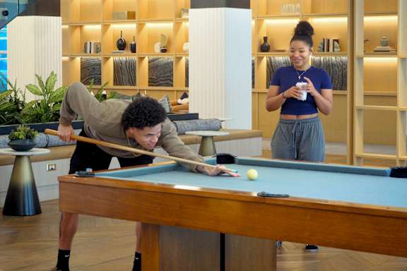 A man is playing pool while a woman stands nearby.