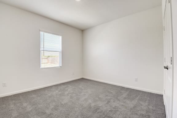 a spacious bedroom with one window, white walls and carpet