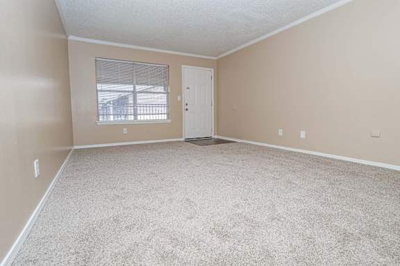 A living room with a carpeted floor and a window with blinds  at The Creole Apartments in Shreveport, LA