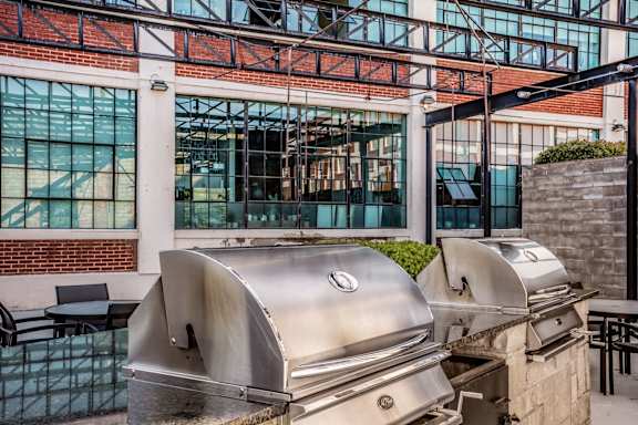 an outdoor patio with two bbq grills and a building in the background