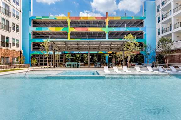 Resort-style swimming pool with in-pool white lounge chairs and parking garage in background at Era Apartments in Denton, TX