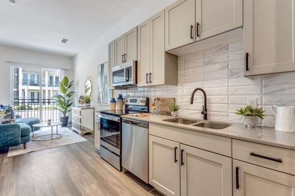 Model Studio kitchen with white cabinets and a sink and stainless steel appliances at Era Apartments in Denton, TX