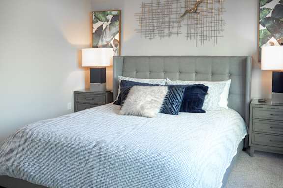 3 bedroom model master bedroom with a bed with pillows and a grey headboard at The Hamilton apartments in Dallas, TX