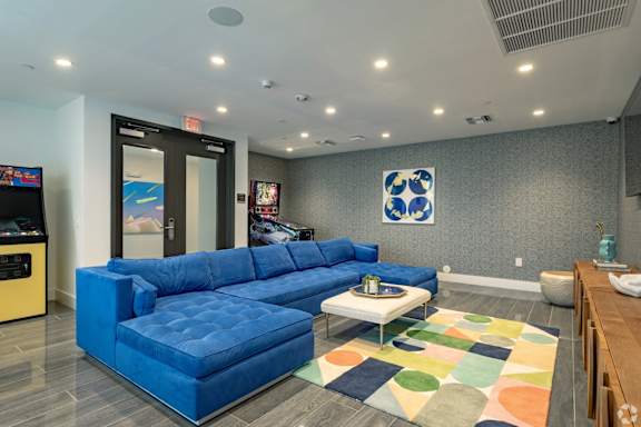 Our lounge and gaming zone with a blue sofa and arcade games at Hollywood Heights on the Boulevard Luxury Apartments in Hollywood, FL
