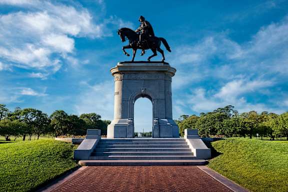A statue of a man on a horse is positioned on a pedestal in front of a large arch.
