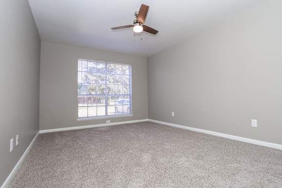 A bedroom with a ceiling fan, large window, and lush carpet at Orleans Square in Shreveport, LA