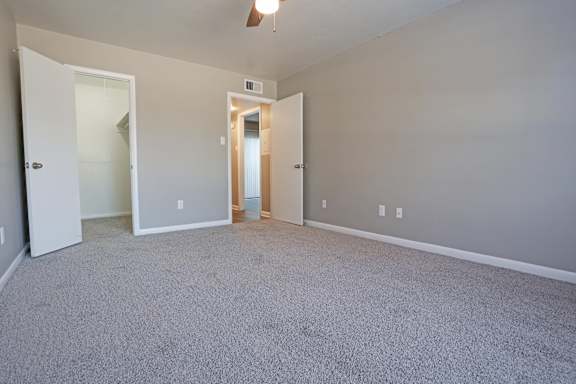 A room with a carpeted floor, ceiling fan, and gray walls at Orleans Square in Shreveport, LA
