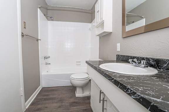 A bathroom with a marble counter, toilet, sink, and tub at Orleans Square in Shreveport, LA