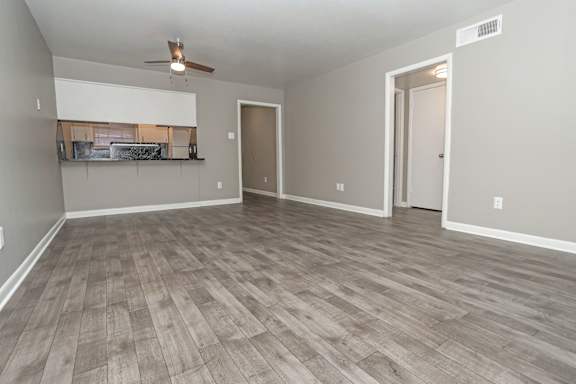 A living room with a ceiling fan and light, and a wooden floor at Orleans Square in Shreveport, LA