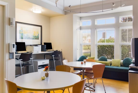 Business center with two computer stations, round tables, and bay window with aqua marine colored cushioning in Wynnfield Lakes apartments in Jacksonville, FL