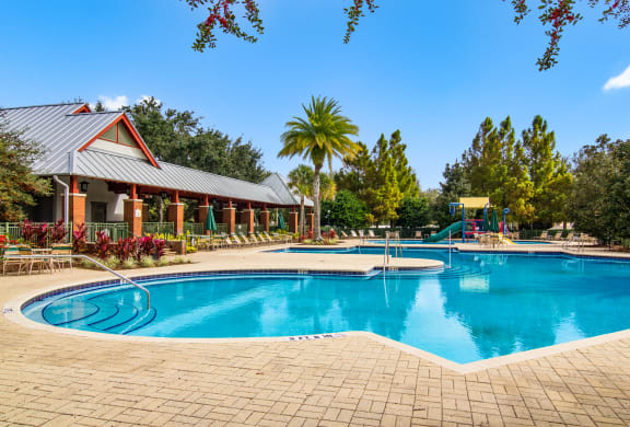 Sparkling pool with lounge chairs and splash park in the background in Wynnfield Lakes apartments in Jacksonville, FL