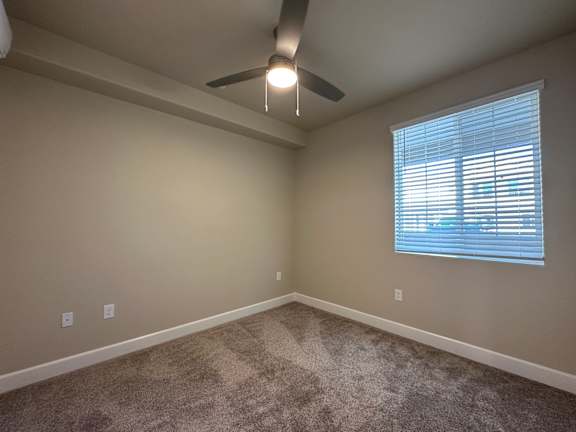 A room with a carpeted floor and a ceiling fan.
