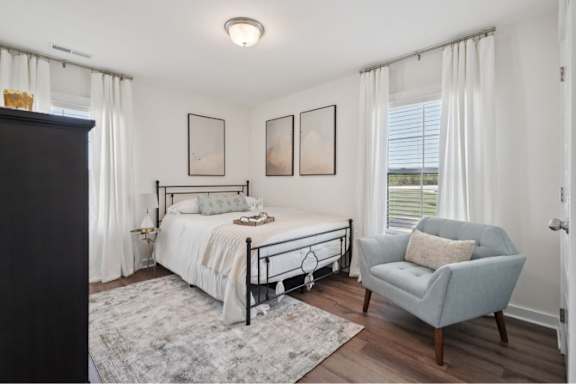 A bedroom with a bed, chair, and pictures on the wall.