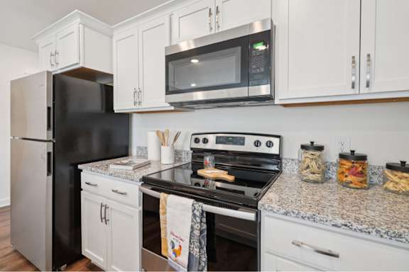 A black refrigerator sits next to a black stove in a kitchen with white cabinets.