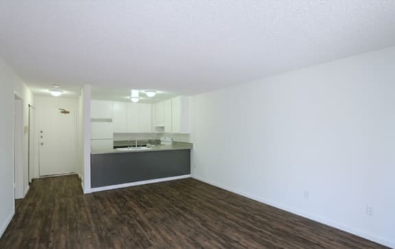 an empty living room with a kitchen in the background