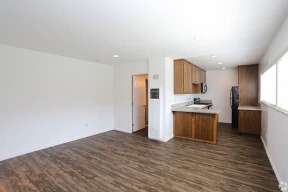 an empty living room with a kitchen in the background