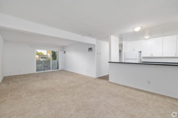 the living room and kitchen of an apartment with white walls and carpet