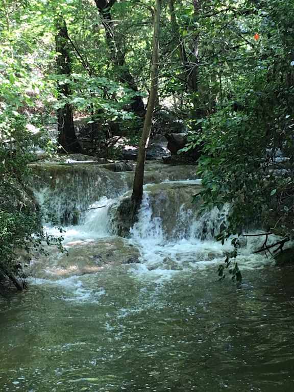 Natural waterfall surrounded by lush greenery at Skyline at Barton Creek Apartments, Austin, TX 78758