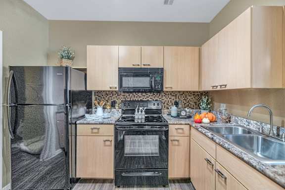 a kitchen with wood cabinets and black appliances and a stainless steel refrigerator at Montage at Pecos Ranch Apartments, Chandler, Arizona