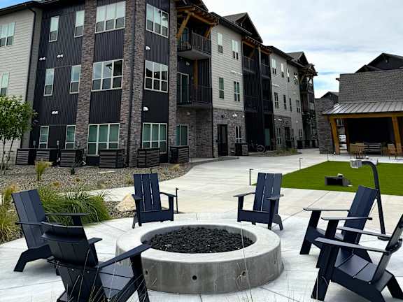 A fire pit surrounded by black chairs in front of a building.