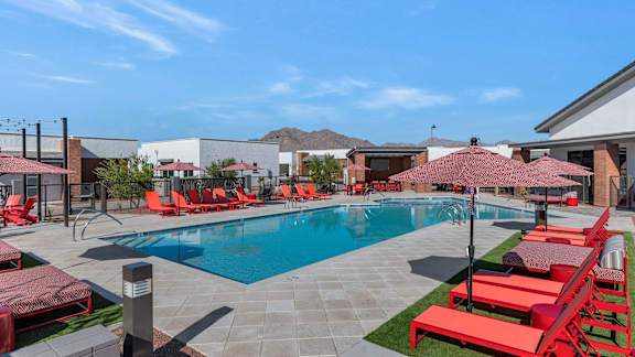 a swimming pool with red chairs and umbrellas in front of a building at Marketside Villas at Verrado, Buckeye, 85396