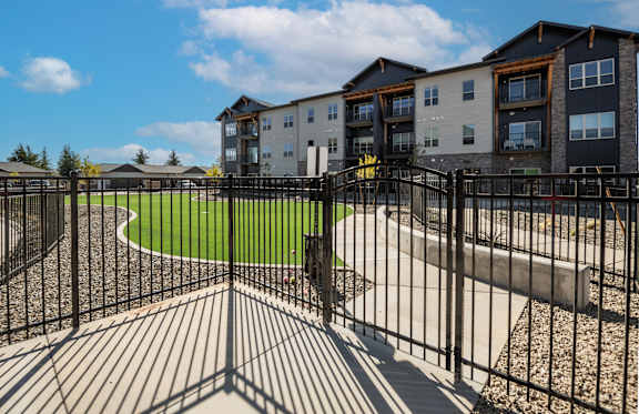 A black metal fence surrounds a playground area in front of apartment buildings at The Crossings  at Windsong, Prescott Valley, 86314
