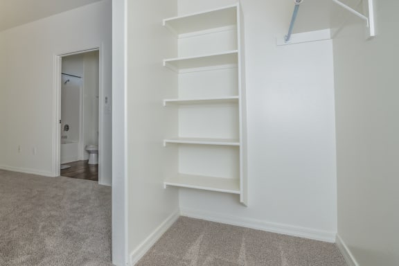 an empty closet with white shelves and a door to a bathroom