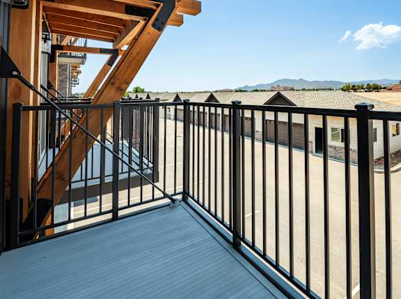 A wooden deck with a metal railing and a staircase leading to a balcony.