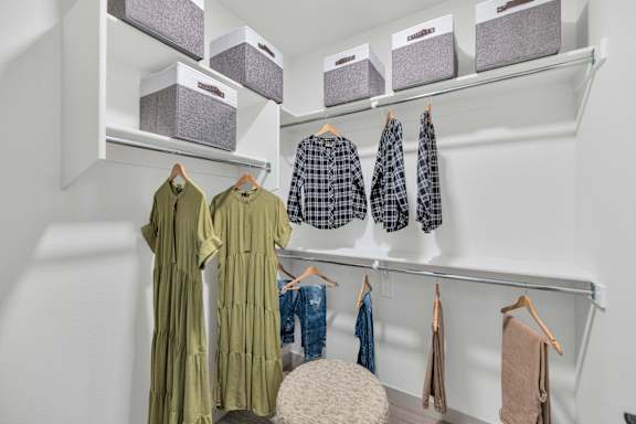 A white closet with clothes hanging and boxes on the shelf.