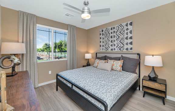 A bedroom with a large bed, a ceiling fan, and a view of the outdoors through the window.