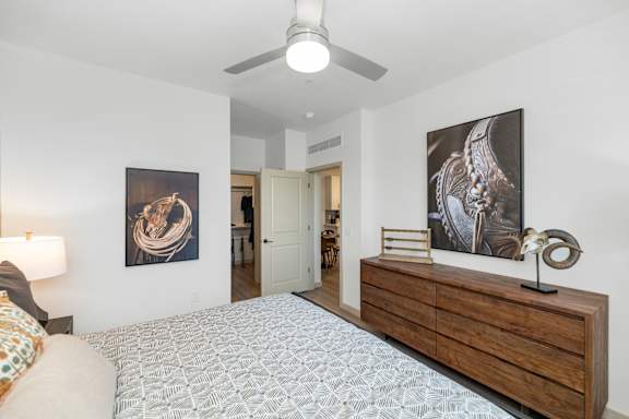 A bedroom with a bed, a ceiling fan, and two paintings on the wall.