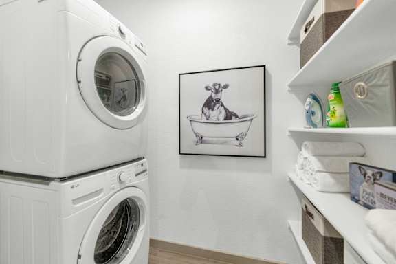 A laundry room with a washing machine and a shelf with towels and detergent.