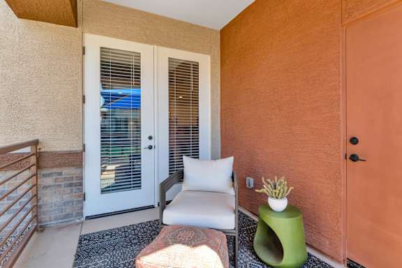 A balcony with a white chair, a green stool, and a white pillow.