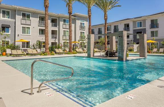 A swimming pool in front of apartment buildings with palm trees.