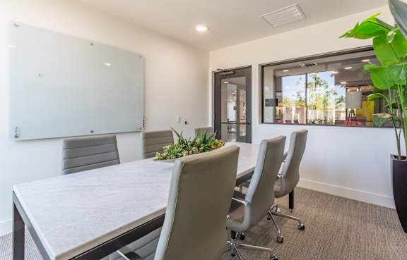 A conference room with a whiteboard, grey chairs, and a table with a plant on it.
