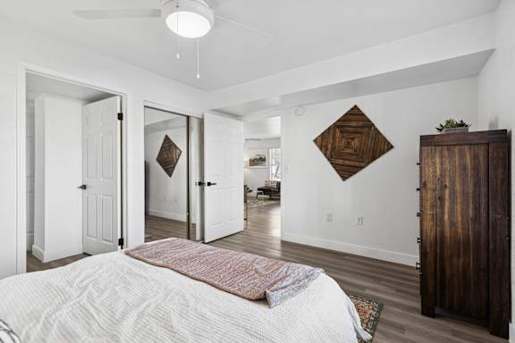 A bedroom with a bed, a ceiling fan, and a wooden cabinet.