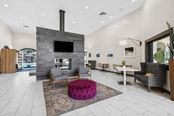 A modern living room with a stone fireplace and a purple ottoman.