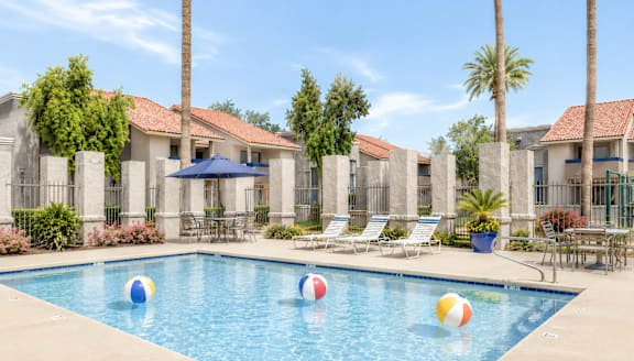 A pool with a blue umbrella and four beach balls.