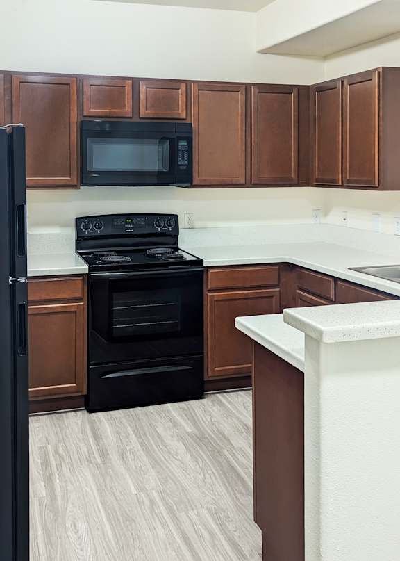 A black refrigerator stands next to a black stove in a kitchen with brown cabinets.