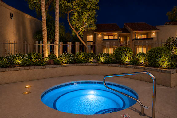 A pool lit up at night with a house in the background.