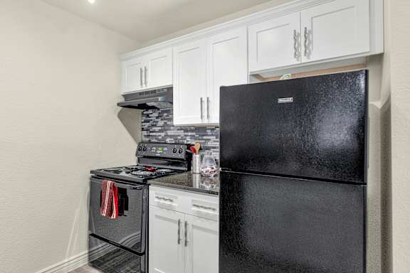 A black fridge sits next to a stove in a kitchen at Urban WalkApartments on 6th Avenue, Phoenix, Arizona