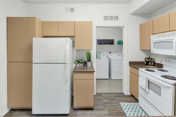 A white refrigerator is in a kitchen with tan cabinets.