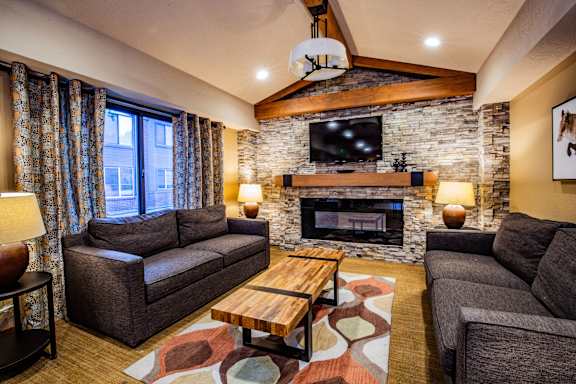 A living room with a stone fireplace and a flat screen TV mounted above it.