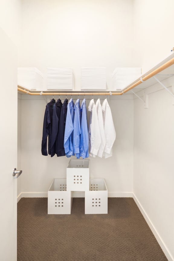 a walk in closet with white crates and clothes hanging on a rack