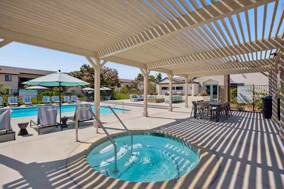 A pool area with a sun shade and a hot tub.