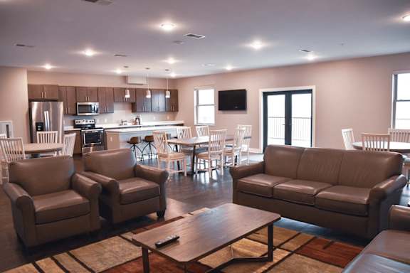 A modern living room with brown leather furniture and a kitchen in the background.