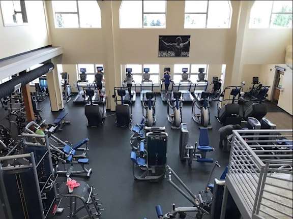 A gym with a variety of exercise equipment and people working out.